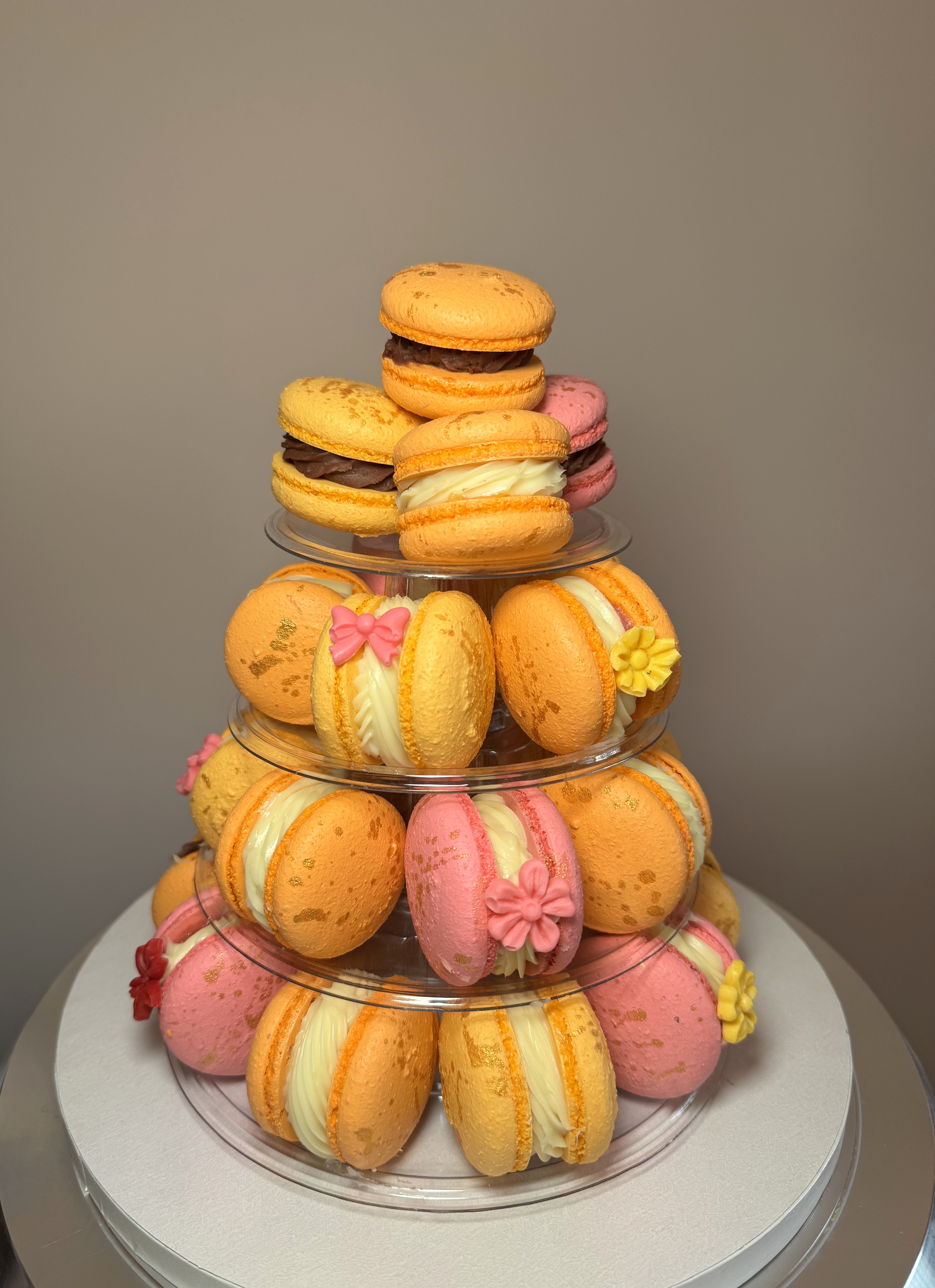 A tiered stand filled with orange, yellow and pink macarons decorated with sugar flowers
